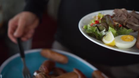 el hombre pone salchichas y hamburguesas en su plato saludable con huevos y ensalada