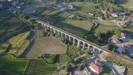 toma de órbita aérea del antiguo puente ferroviario de arco proyectando sombra en el campo de maíz al atardecer - ponte seca, durrães, barcelos