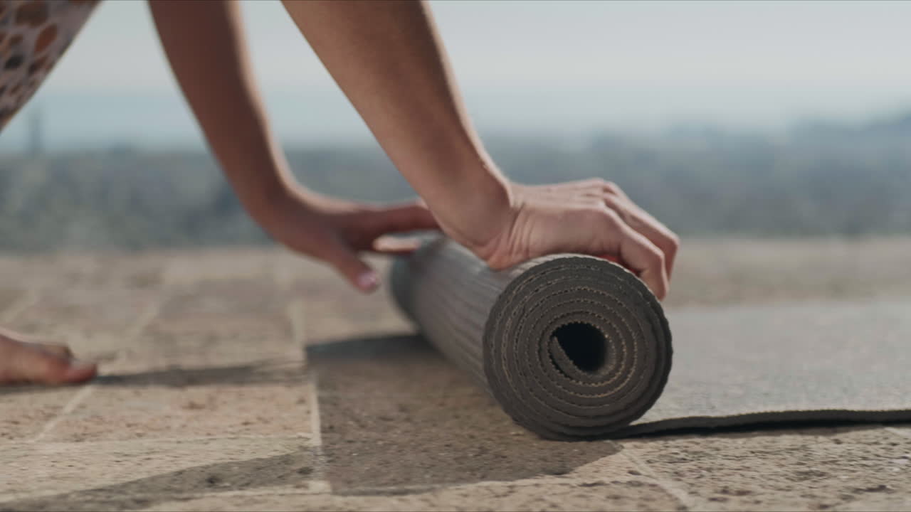 las manos de la mujer enrollando la alfombra de yoga después del entrenamiento. niña plegando la alfombrilla de fitness al aire libre