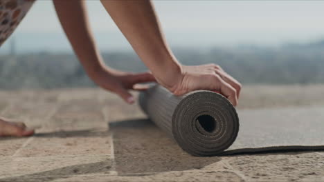 woman hands rolling up yoga mat after training.girl folding fitness mat outdoors