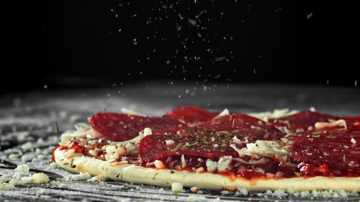 Movimento rallentato di erbe aromatiche cosparse su una pizza con salame piccante cruda