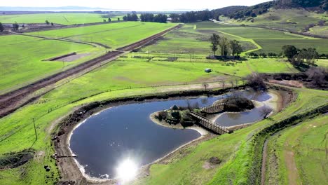 aerial flyover of small farm and pond with gazebo and sun reflecting in the pond