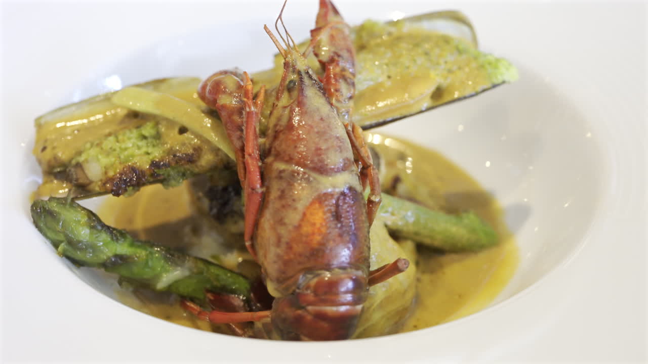 Close up of whole cooked crayfish with a mussel shell filled and a creamy herb topping on a white plate