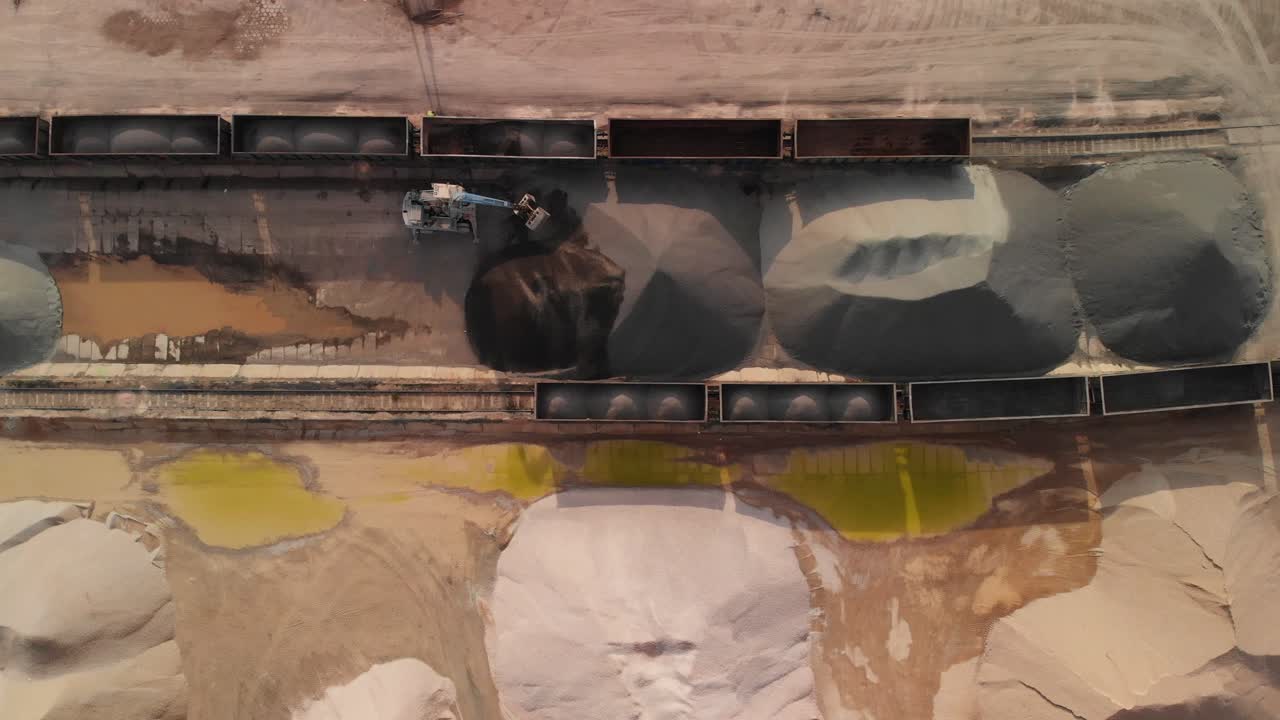 Aerial top down shot o an excavator unloading gravel from wagon in a rail gravel terminal
