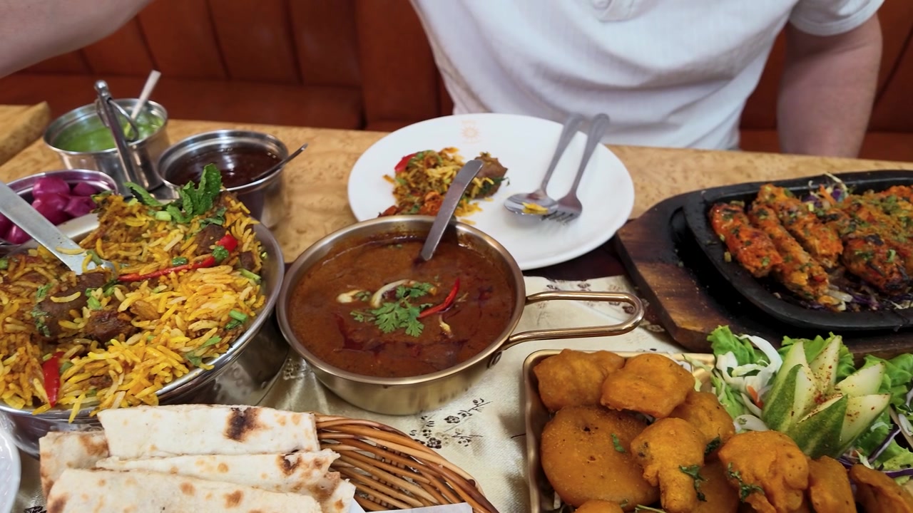 Et udvalg af traditionelle indiske retter, herunder karry, biryani og samosaer, serveret på en restaurant.