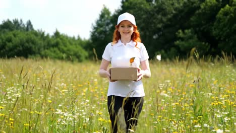 a woman with orange hair holds a package while surrounded by colorful wildflowers under a bright sky. butterflies flutter around her as she enjoys the beautiful day outdoors.