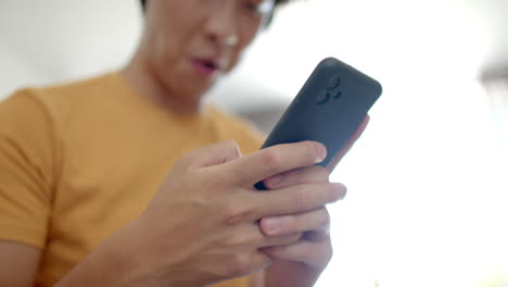 Asian-college-student-looking-at-smartphone,-wearing-orange-shirt