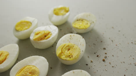 Video-of-close-up-of-peppered-halves-of-hard-boiled-eggs-on-grey-background