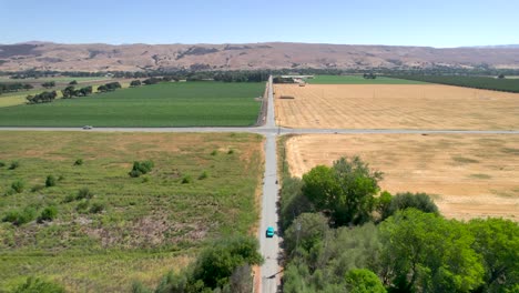Drone-footage-of-light-blue-classic-mustant-driving-down-rural-country-roads-in-California,-during-the-day