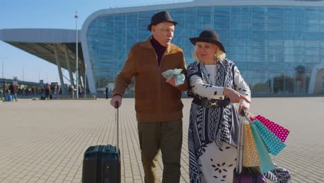 senior rich pensioner tourists walking with shopping bags from vacation holding dollar money cash