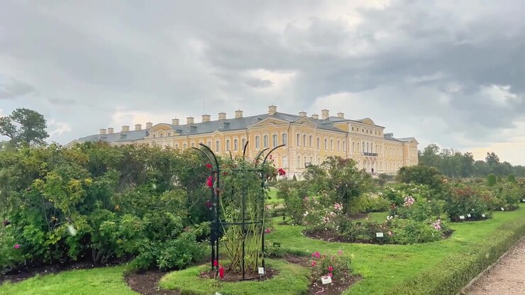 Vista esterna di un grande palazzo giallo caratterizzato da un curato giardino di rose in primo piano. Ideale per documentari di viaggio, promozioni turistiche e media di architettura storica