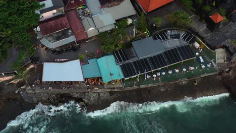 waves crashing at the waters edge with people dinning at echo beach in canggu bali, aerial top down