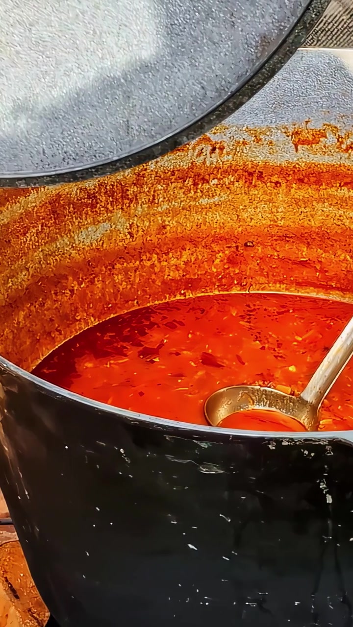 Primo piano verticale di ricco e vivace stufato o salsa di pomodoro rosso che bolle in una pesante pentola nera.