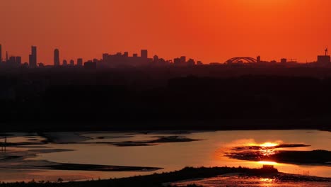 sun setting with bright orange skyline over rotterdam and the calm water of the river noord