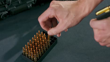 close-up of male hands loading bullets into a gun magazine clip at a firing range