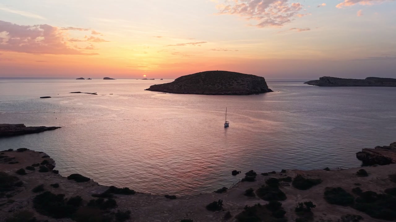 Una barca a vela solitaria riposa vicino a una piccola isola al largo di Ibiza durante un tramonto dorato