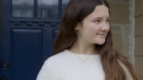 Cute-teenage-girl-on-front-porch-looking-right-smiles-and-looks-into-camera,-handheld-camera-drifts