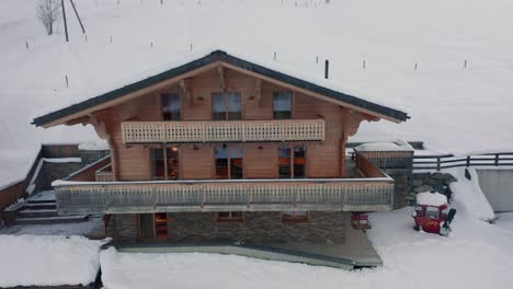 Drone-flying-towards-luxurious-chalet-and-flying-over-snow-covered-roof