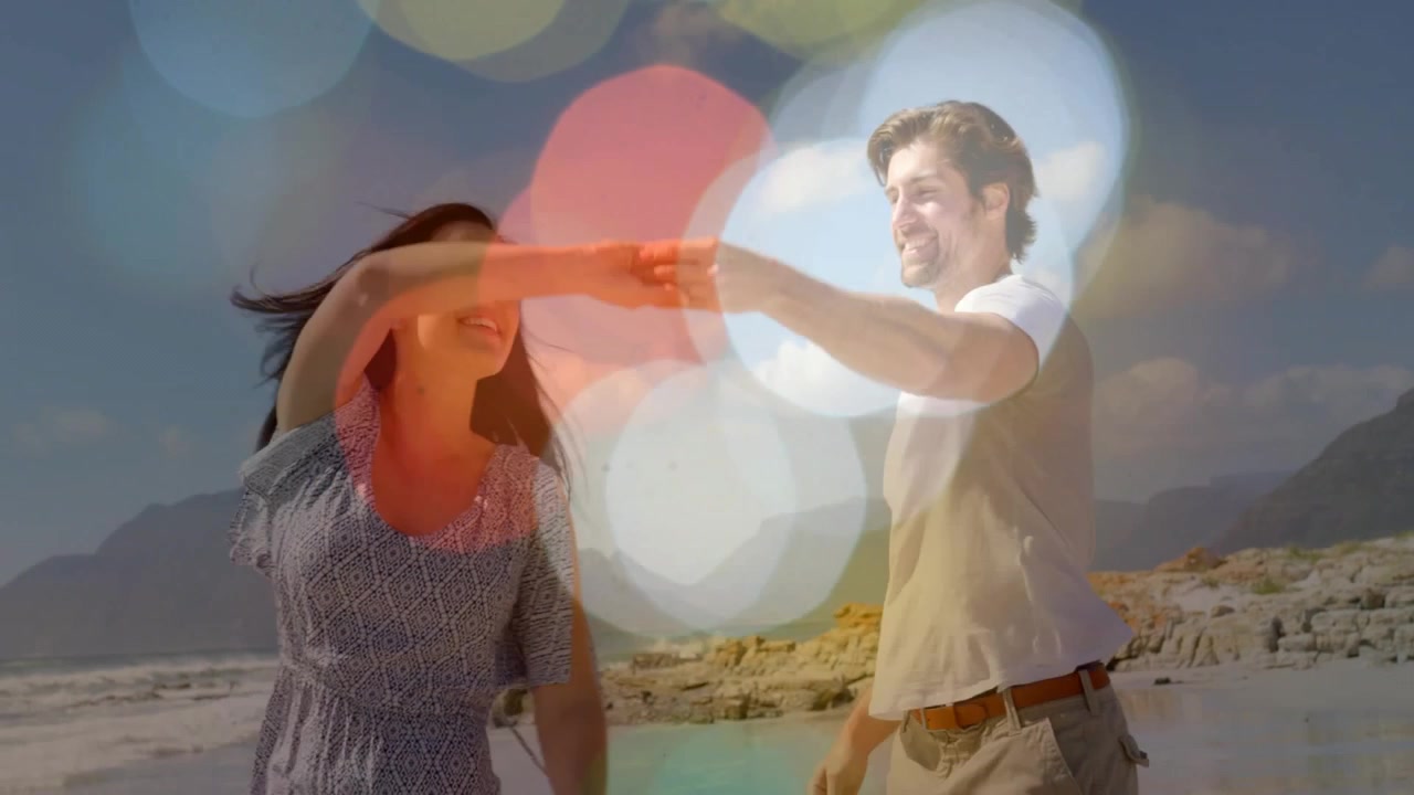 Donna che alza il braccio esortando l'uomo a farla girare, tenendosi per mano e avvicinandosi, con uno sfondo bokeh sulla spiaggia, per annunci divertenti.