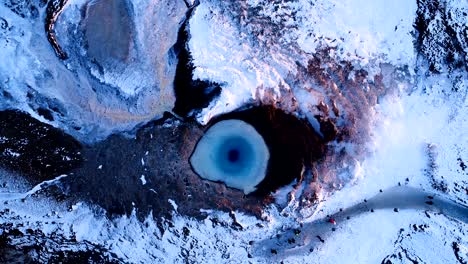 aerial view of a drone which getting further and further of the center of a geuser in geysir, iceland . smoke is getting out of the geyser with people walking all around the geyser, under the red sunset.