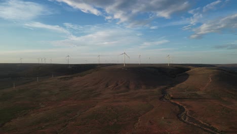 Birdseye-view-of-wind-farm-with-turbines-over-hills-at-sunset,-Australia