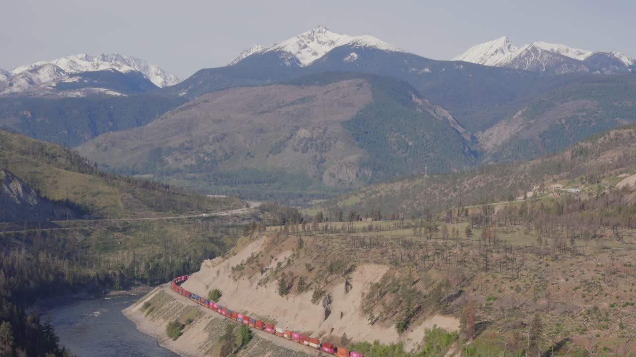 Treno merci che si snoda attraverso il canyon del fiume Thompson in Columbia Britannica, Canada, con cime montuose innevate