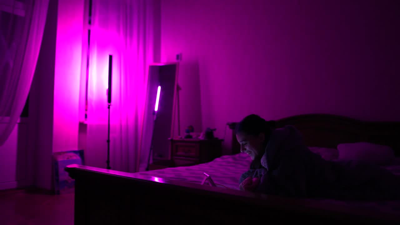 mujer usando tableta en un dormitorio iluminado de púrpura por la noche