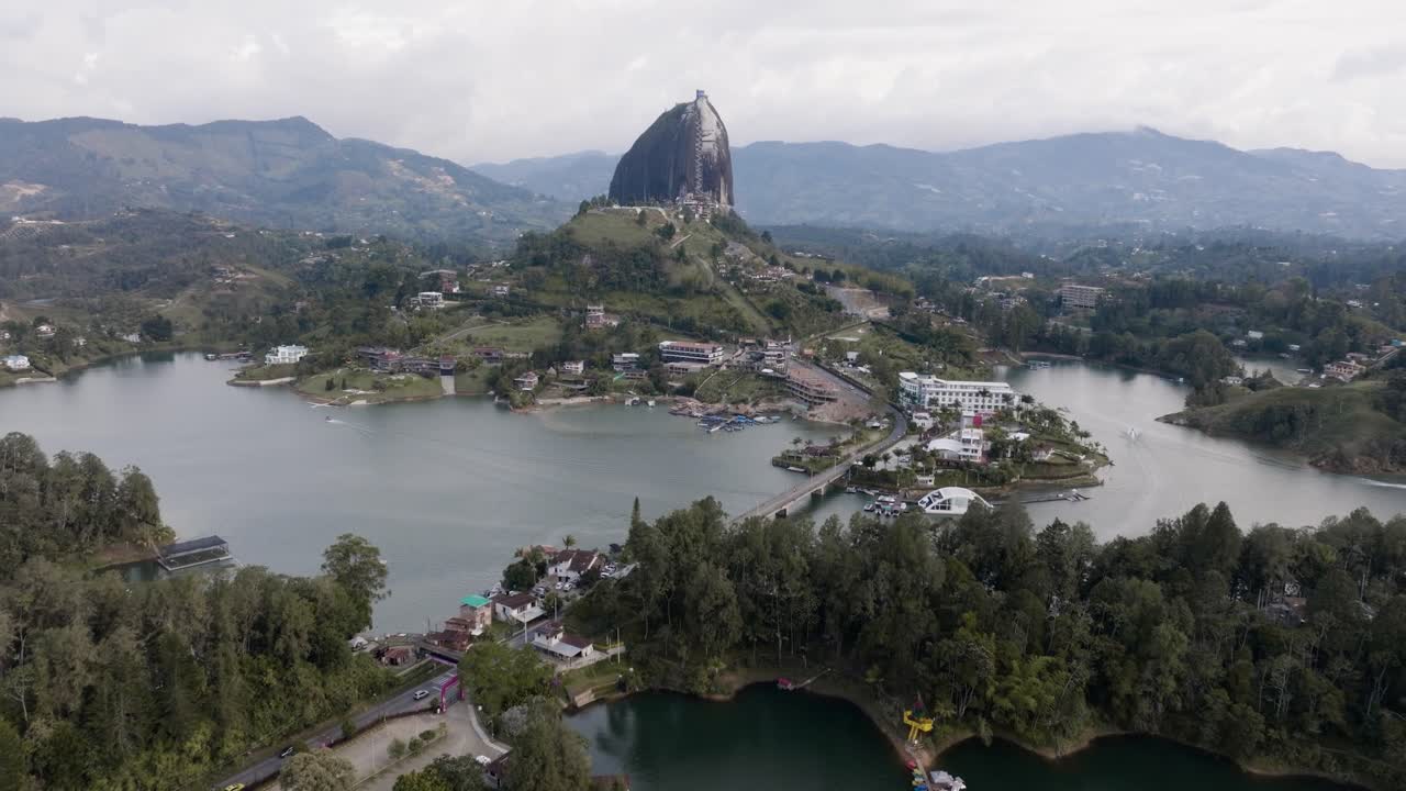 Drone shot approaching El Peñón de Guatapé (La Piedra Rock) with lakes and mountains on a cloudy day