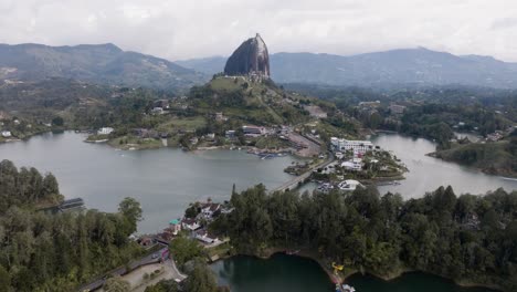 drone shot approaching el peñón de guatapé (la piedra rock) with lakes and mountains on a cloudy day