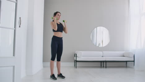 Home-exercises-for-a-beautiful-body-a-young-brunette-woman-lifts-dumbbells-in-her-arms-up-in-slow-motion.