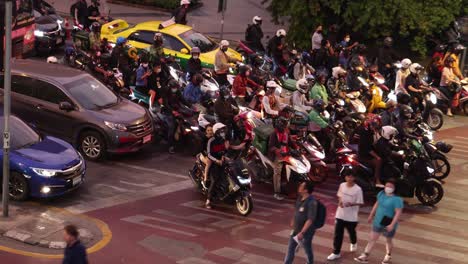 motocicletas y coches navegan por un cruce de peatones lleno de gente.