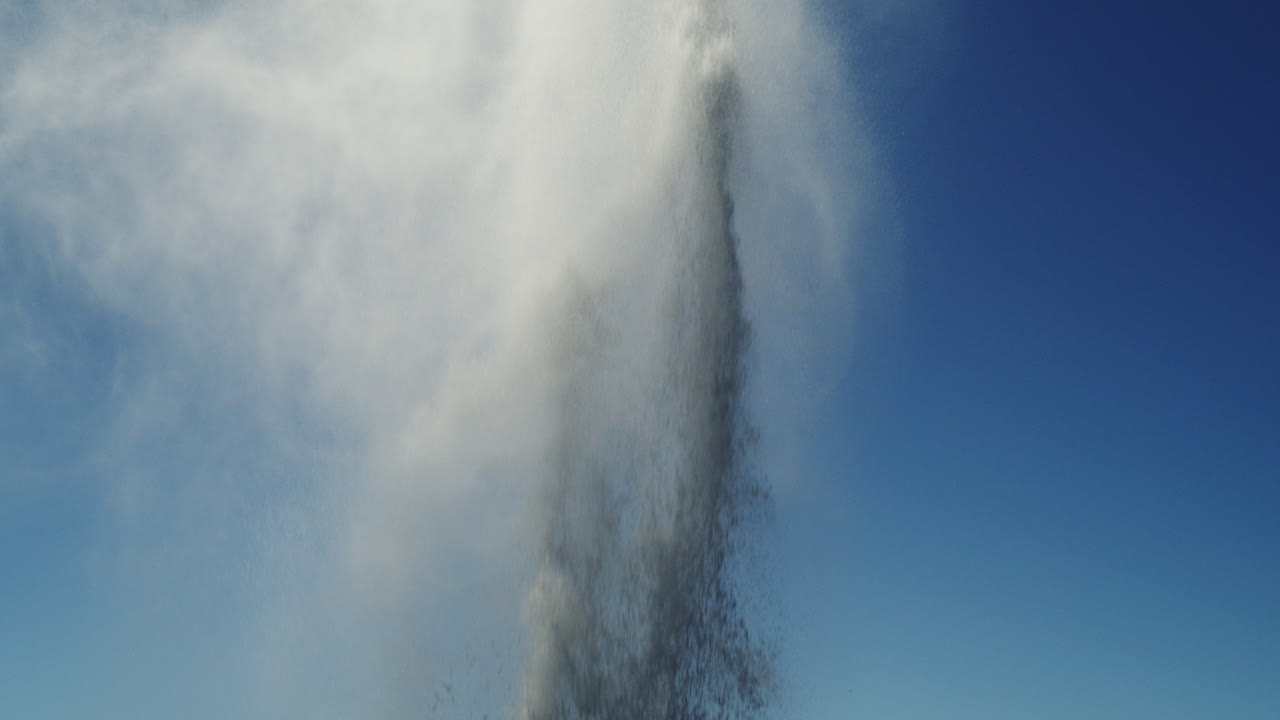 Thin stream of ocean vapor shoots up against clear blue sky in slow-motion cinematic shot