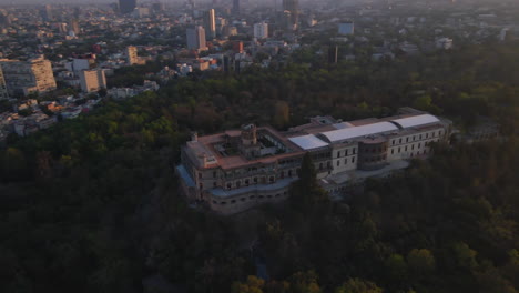 Cinematic-aerial-Mexico-City-Castle-with-tower-in-middle-and-flag,-surrounded-by-Chapultepec-forest-and-cityscape-background