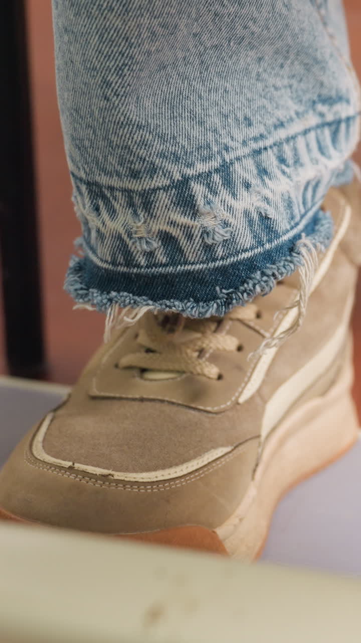 primo piano di una sneaker che preme un pedale, scarpa da ginnastica scamosciata color cuoio sotto un orlo di jeans sfilacciato, musicista che preme un pedale per effetti di chitarra, pavimento caldo di uno studio, ritmo intimo al rallentatore, dettaglio autentico di uno stile di vita