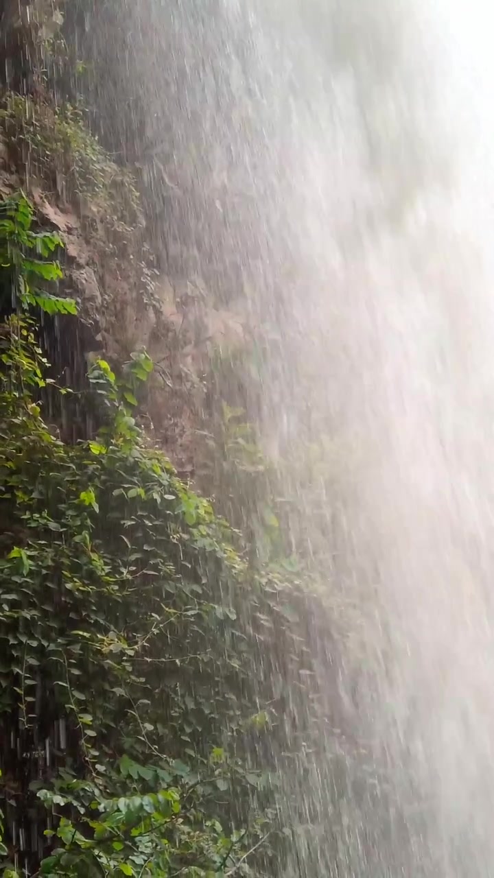 Vista em close de uma poderosa cachoeira fluindo por um penhasco rochoso, com água branca em movimento rápido, superfície de rocha molhada e vegetação verde visível ao longo da floresta circundante