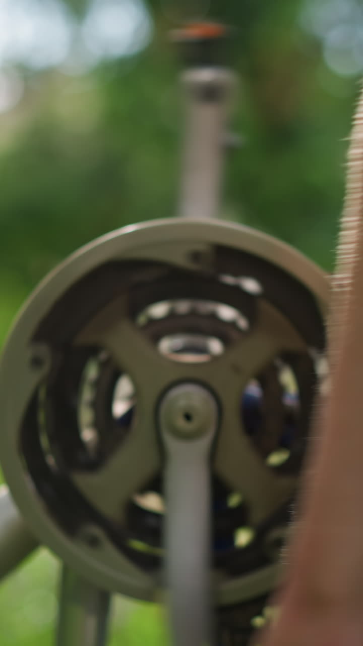 primer plano de la mano girando la rueda de la bicicleta mientras se centra en la cadena y el sistema de engranajes, la vegetación en el fondo proporciona un efecto suave y borroso con las hojas moviéndose ligeramente