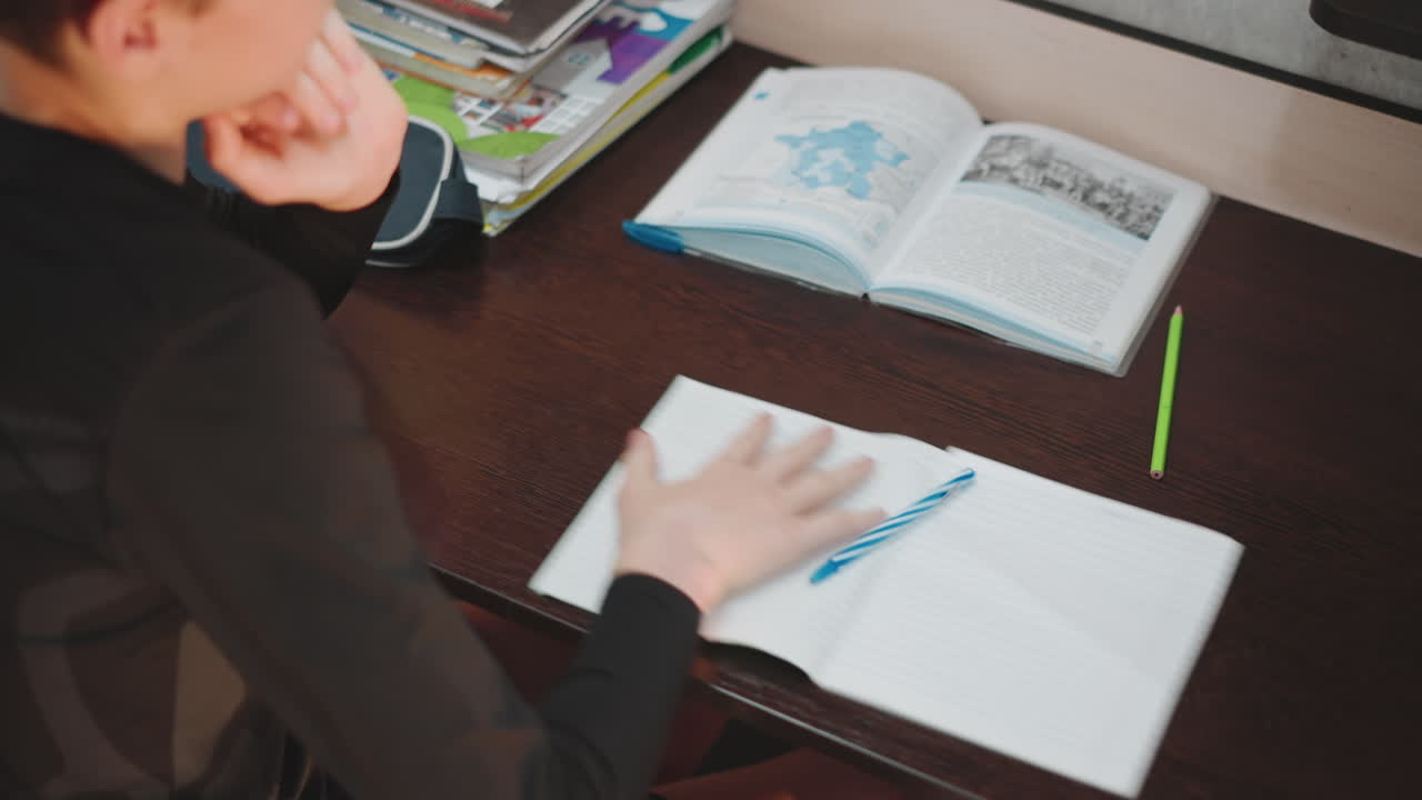 Un giovane ragazzo esamina intensamente il suo quaderno di esercizi, completamente concentrato sul materiale di lettura educativo e sulle forniture per l'apprendimento che lo circondano.