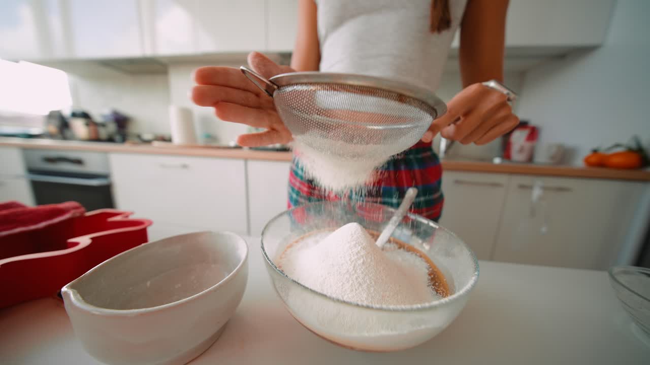 Woman sifting flour into a bowl in the kitchen