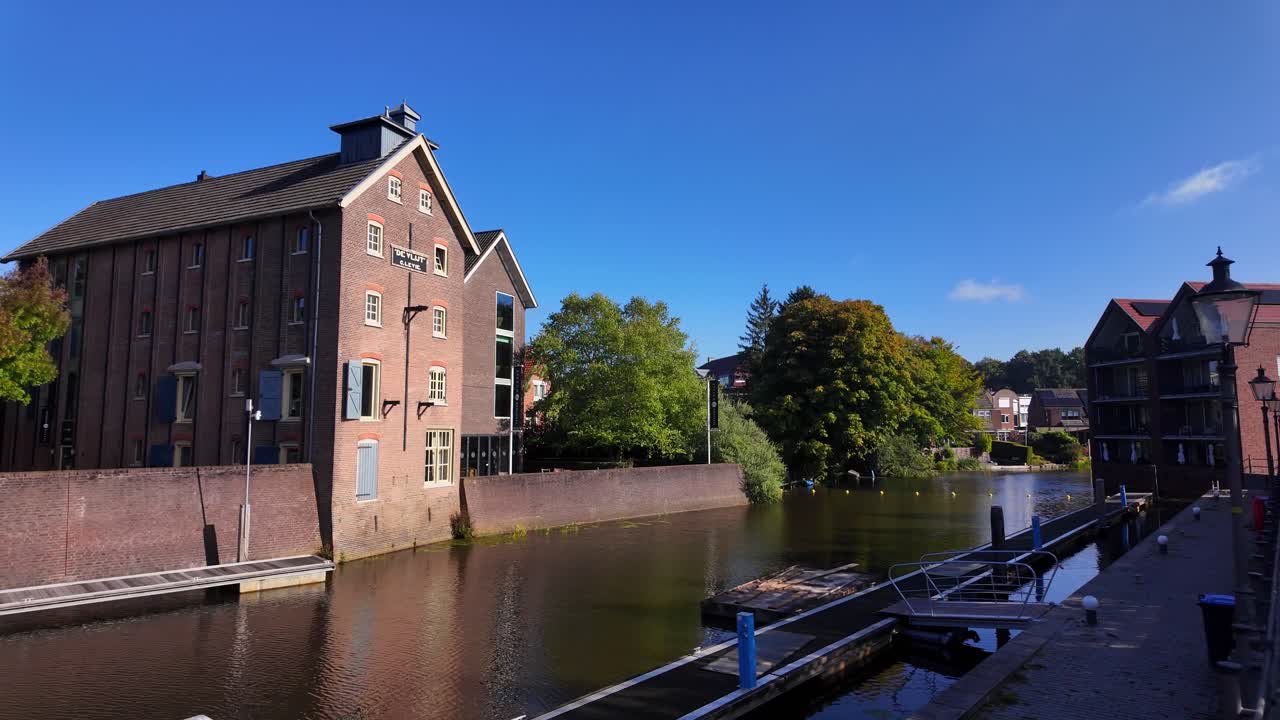 Historic warehouse with red brick facade and shutters standing beside calm canal water under blue sky in Coevorden, Drenthe. Location: Coevorden, Netherlands – Coevorden, Nederland