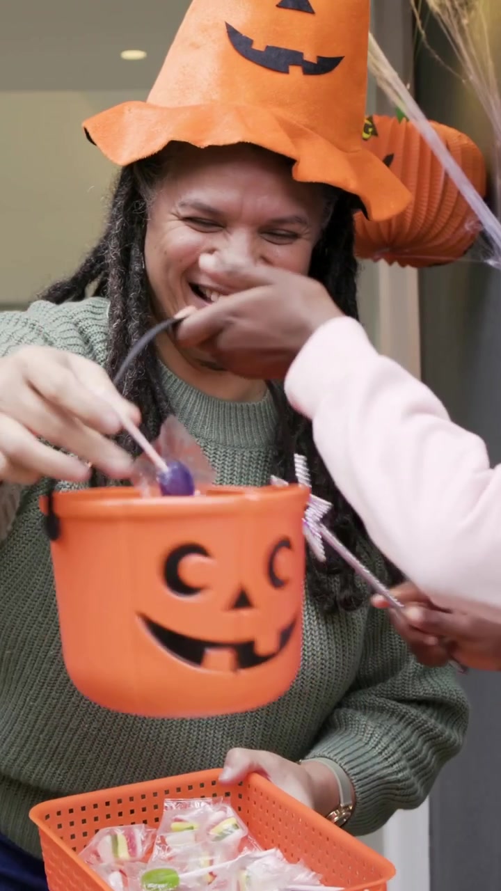 Bambini che si avvicinano all'ingresso, una coppia di padroni di casa distribuisce caramelle da un cesto arancione, festeggiando Halloween.