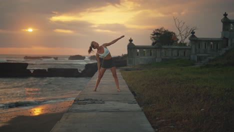 woman doing yoga on bali shore at sunset performing triangla pose, asana