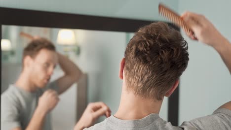 portrait in the mirror of a young man combing his hair with a wooden comb