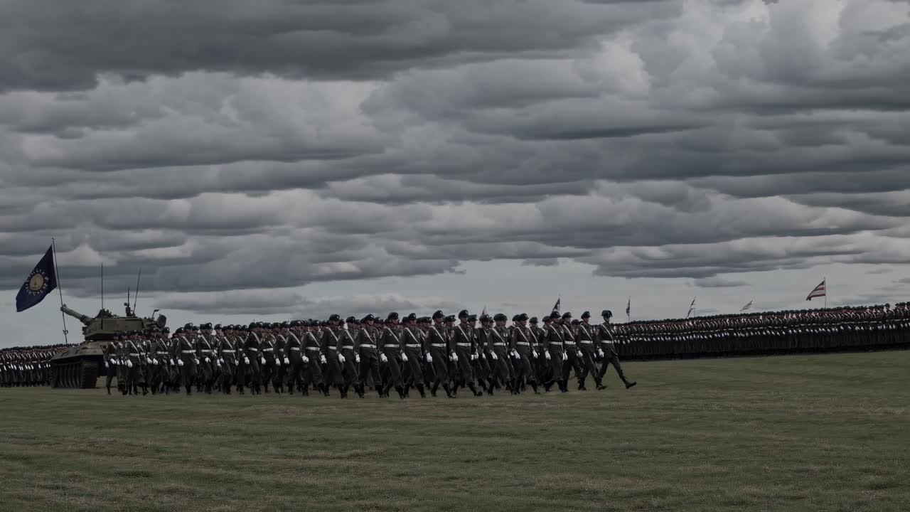 A dramatic, wide-angle video shot of soldiers marching in formation under a cloudy sky