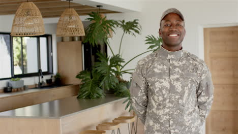 smiling african american man in military uniform standing in modern kitchen, looking confident