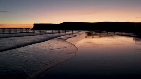 saltburn by the sea and pier - resplandor naranja temprano en la mañana - 4k prores 422 - drone se mueve hacia y sobre el muelle hacia huntcliff