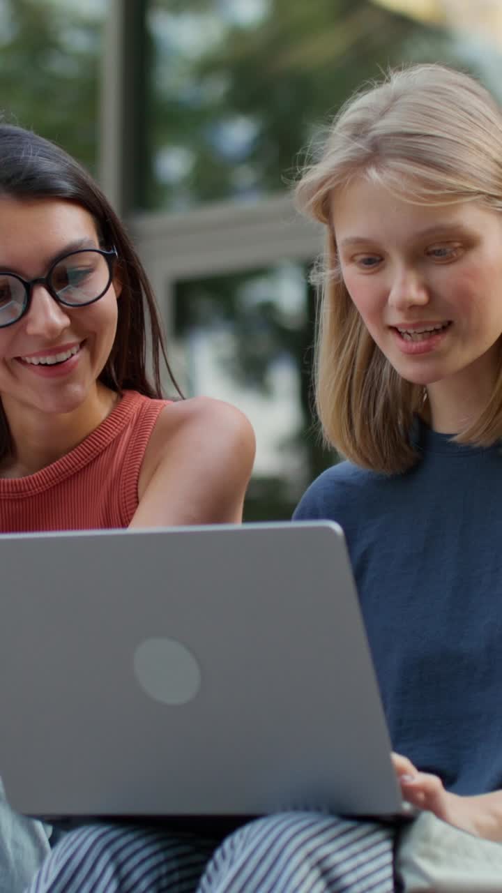 To unge kvinder samarbejder på en bærbar computer udendørs