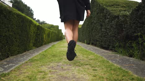 beautiful model has a great body walking in green maze with her jacket open looking at her hand following footpath slow motion cloudy settings