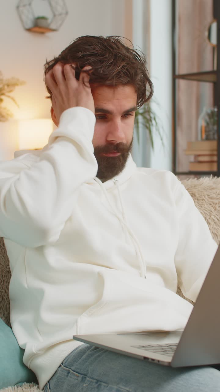 Giovane uomo indiano freelance turbato seduto sul divano di casa che usa il portatile, in preda ad ansia e stress