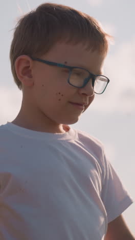 un primer plano de un niño con gafas y una camisa blanca, sosteniendo la mano de su madre. la madre, parcialmente visible, está llevando una canasta llena de mercancías, caminando