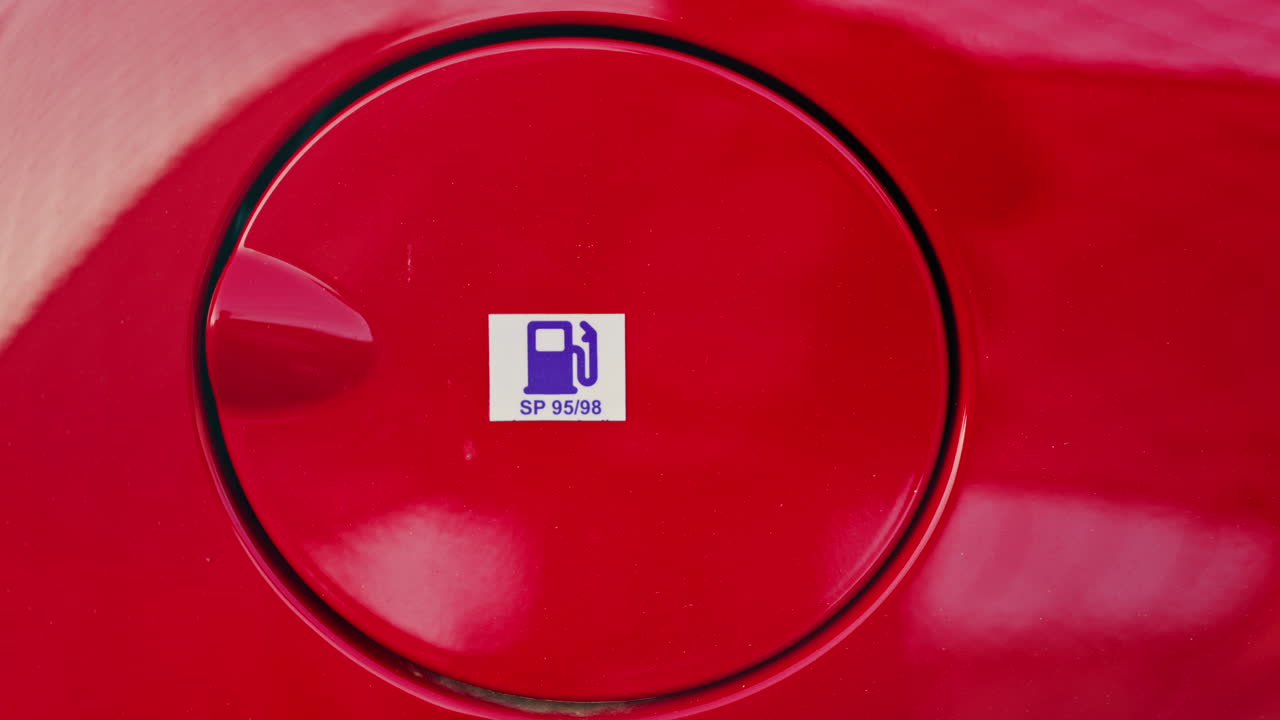 Close up of the fuel door of a red car with a sticker on it